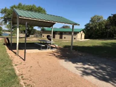 Grill, fire ring, and covered picnic table with restroom/shower facilities in the background