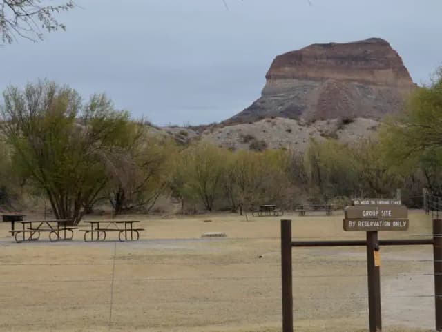 Group campsite sits among the desert brush in a fenced in area with a desert bluff in the background