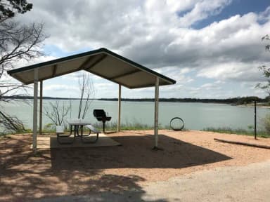 Covered picnic table, grill, and fire ring with Waco Lake in the background