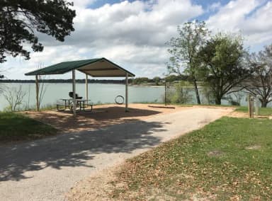 RV site with covered picnic table, grill, fire ring, and Waco Lake in the background