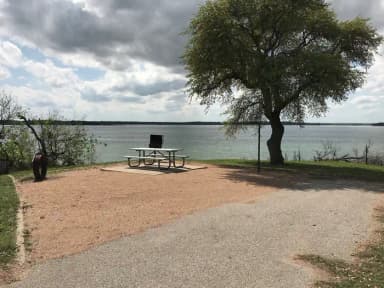 Picnic table, grill, and fire ring with Waco Lake in the background