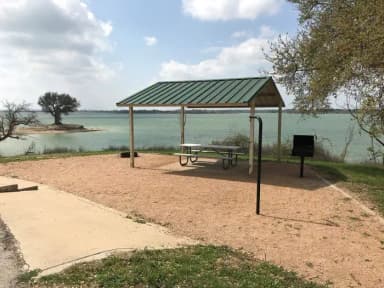 Picnic table, grill, and fire ring with Waco Lake in the background