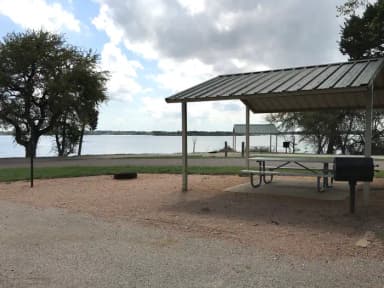 Covered picnic table, grill, and fire ring with Waco Lake in the background