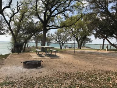 Picnic table, grill, and fire ring with Waco Lake in the background
