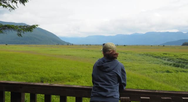 Visitor on porch of Little Dry Island Cabin looking out to grassflats and mountains in background
