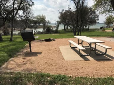 Picnic table, grill, and fire ring with Waco Lake in the background
