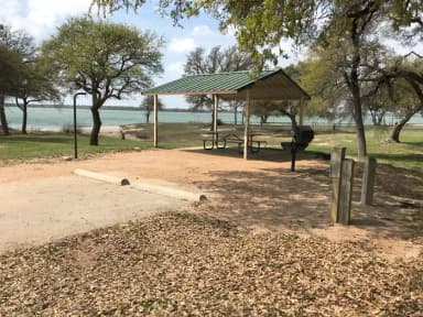 RV site with covered picnic table, grill, fire ring, and Waco Lake in the background