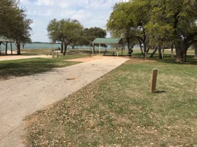 RV site with covered picnic table, grill, fire ring, and Waco Lake in the background