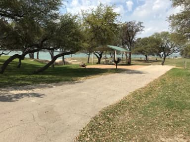 RV site with covered picnic table, grill, fire ring, and Waco Lake in the background