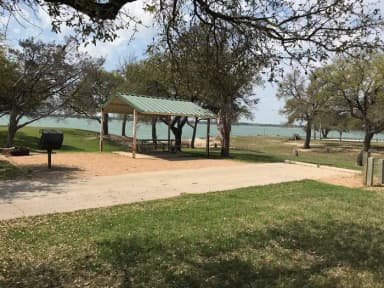 RV site with covered picnic table, grill, fire ring, and Waco Lake in the background