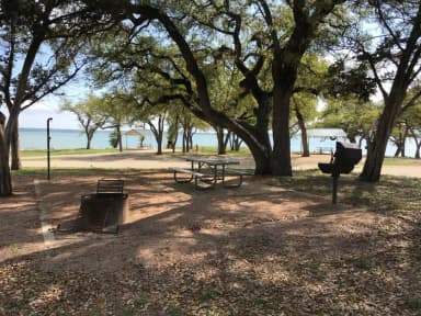 Picnic table, grill, and fire ring with Waco Lake in the background