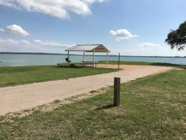 RV site with covered picnic table, grill, fire ring, and Waco Lake in the background