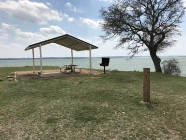 Tent site with covered picnic table, grill, and fire ring.  Site is located very close to shoreline of Waco Lake