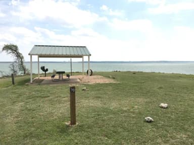 Tent site with covered picnic table, grill, and fire ring.  Site is located very close to shoreline of Waco Lake