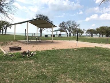 RV site with covered picnic table, grill, fire ring, and Waco Lake in the background