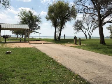 RV site with covered picnic table, grill, fire ring, and Waco Lake in the background