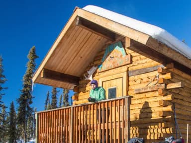 A woman looks out from the front deck of a log cabin.
