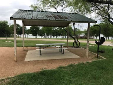 Covered picnic table, grill, and fire ring with Waco Lake in the background
