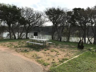 Picnic table, grill, and fire ring with Waco Lake in the background