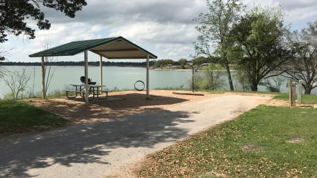 RV site with covered picnic table, grill, fire ring, and Waco Lake in the background