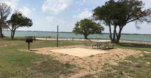 Tent site with picnic table, grill, fire ring, and Waco Lake in the background