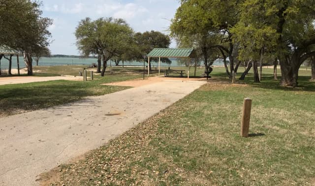 RV site with covered picnic table, grill, fire ring, and Waco Lake in the background