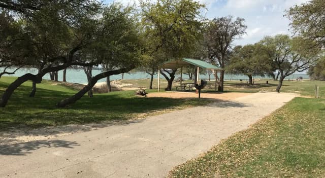 RV site with covered picnic table, grill, fire ring, and Waco Lake in the background