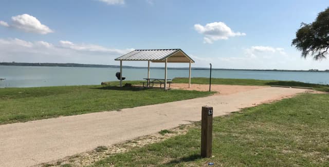 RV site with covered picnic table, grill, fire ring, and Waco Lake in the background