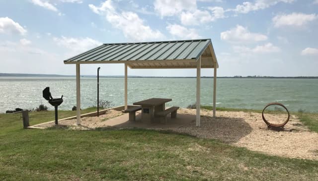 Tent site with covered picnic table, grill, and fire ring.  Site is located very close to shoreline of Waco Lake