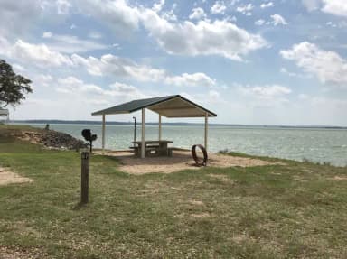 Tent site with covered picnic table, grill, and fire ring.  Site is located very close to shoreline of Waco Lake