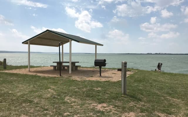 Tent site with covered picnic table, grill, and fire ring.  Site is located very close to shoreline of Waco Lake