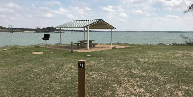 Tent site with covered picnic table, grill, and fire ring.  Site is located very close to shoreline of Waco Lake