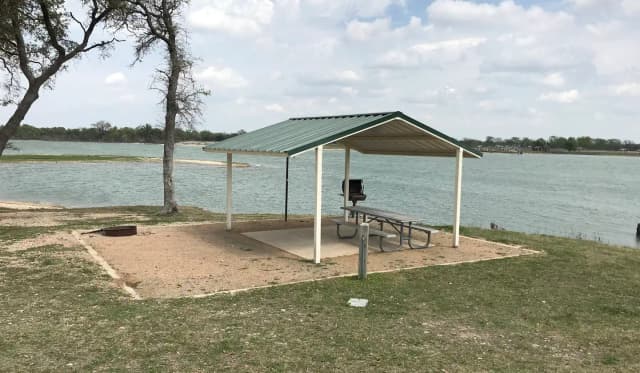 Tent site with covered picnic table, grill, and fire ring.  Site is located very close to shoreline of Waco Lake