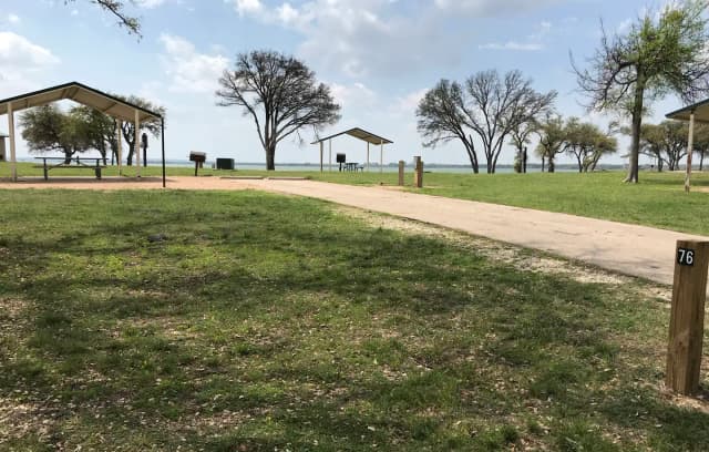 RV site with covered picnic table, grill, fire ring, and Waco Lake in the background