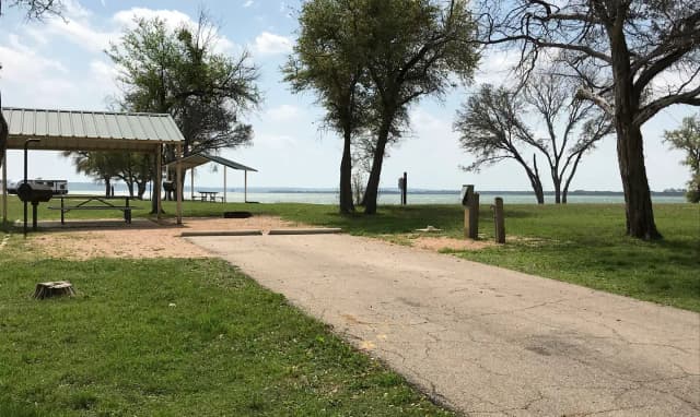 RV site with covered picnic table, grill, fire ring, and Waco Lake in the background