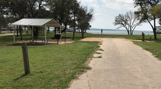 RV site with covered picnic table, grill, fire ring, and Waco Lake in the background