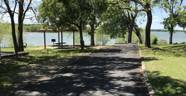 RV site with covered picnic table, grill, fire ring, and Waco Lake in the background