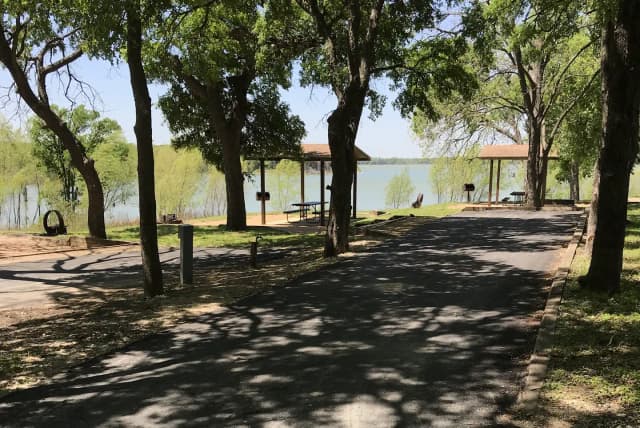 RV site with covered picnic table, grill, fire ring, and Waco Lake in the background