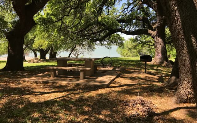 Tent site with picnic table, grill, and fire ring with Waco Lake in the background