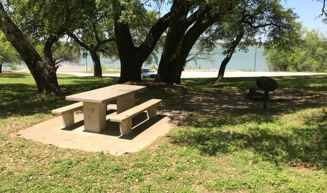 Tent site with picnic table, grill, and fire ring with Waco Lake in the background