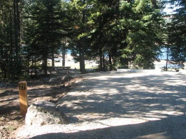 Site 27, campsite surrounded by pine trees, picnic table & fire ring