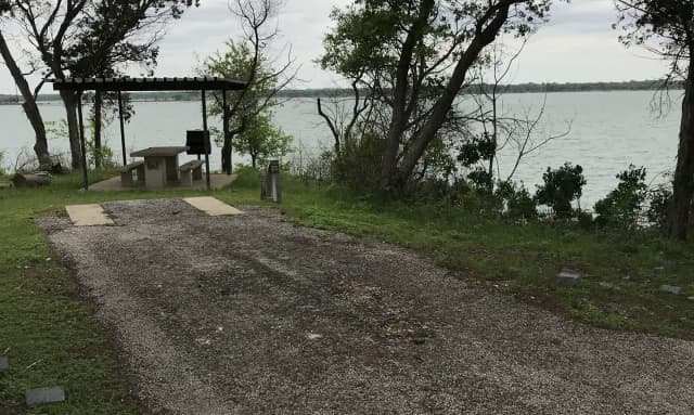 RV site with covered picnic table, grill, fire ring, and Waco Lake in the background