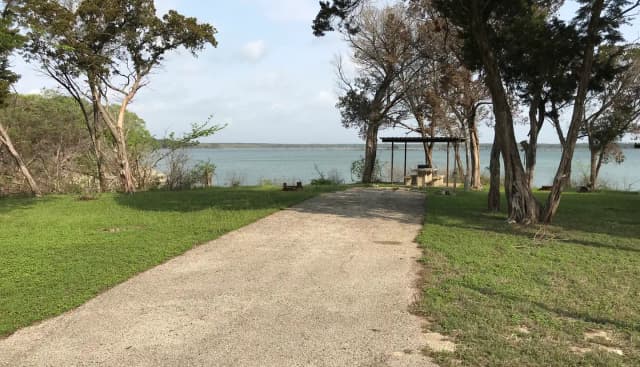 RV site with covered picnic table, grill, fire ring, and Waco Lake in the background
