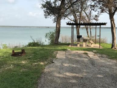 RV site with covered picnic table, grill, fire ring, and Waco Lake in the background