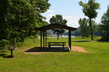 Alder shelter, with picnic tables and grill at Otter Brook Lake, with the lake in the background.