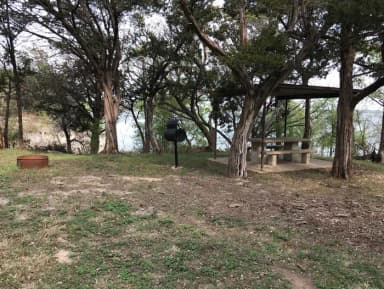 Covered picnic table, grill, and fire ring at site with Waco Lake in the background