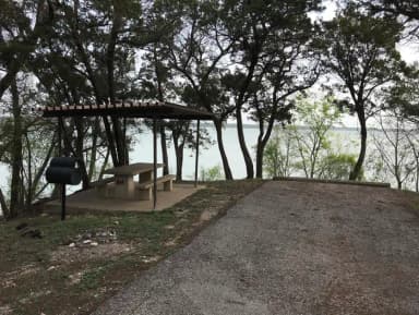 RV site with covered picnic table, grill, and Waco Lake in the background