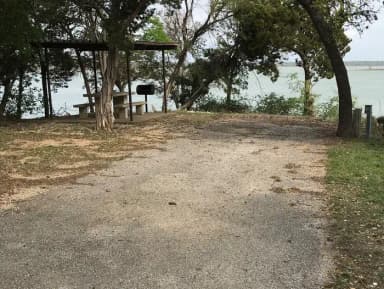 RV site with covered picnic table, grill, and Waco Lake in the background