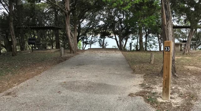 RV site with covered picnic table, grill, and Waco Lake in the background