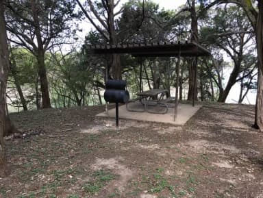 RV site with covered picnic table, grill, and Waco Lake in the background